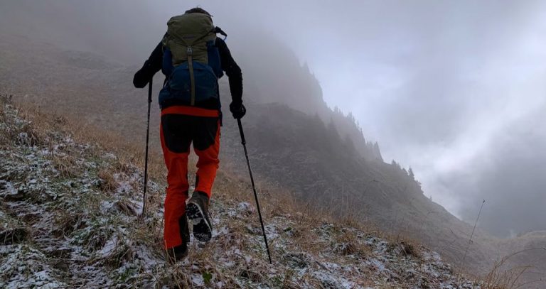 Hombre caminando por una montaña con un par de bastones de senderismo